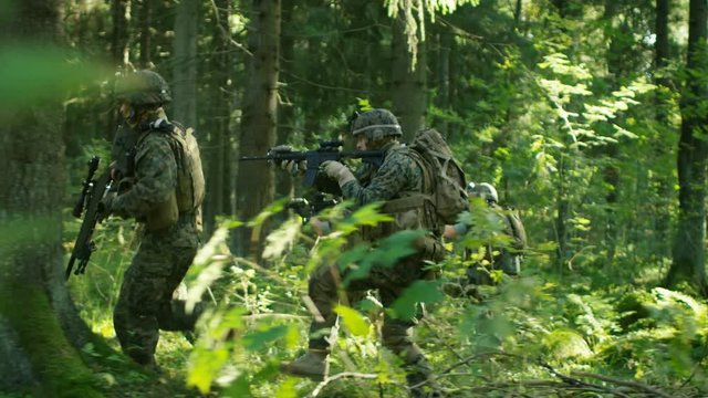 Military Operation in Action, Squad of Five Fully Equipped Soldiers Wearing Camouflage Uniform Attacking Enemy, Rifles in Firing Position. They're Running in Formation Through Dense Forest. 