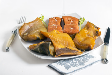 Différents poissons fumés dans une assiette et couvert sur fond blanc