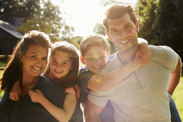 Portrait Of Parents Giving Children Piggyback In Garden