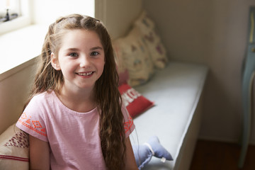Naklejka premium Portrait Of Smiling Young Girl Sitting On Window Seat At Home