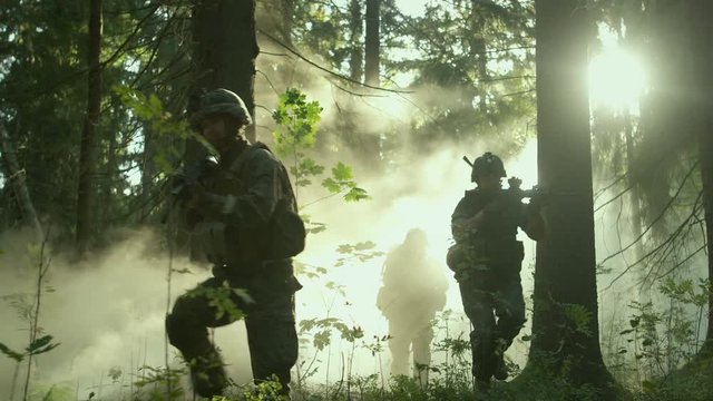 Fully Equipped Soldiers Wearing Camouflage Uniform Attacking Enemy, Rifles Ready to Shoot. Military Operation in Action, Squad Running in Formation Through Dense Smokey Forest. 