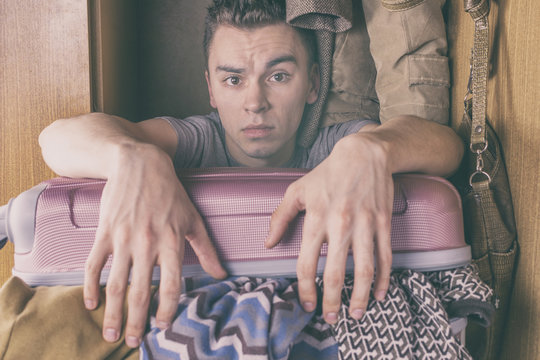 A young man sits with a suitcase of clothes