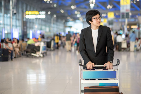 Young asian man with his luggage on airport trolley waiting for check in at airline counter in the international airport terminal, business travel concept