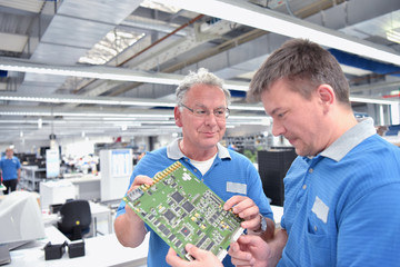 Teamwork: Techniker in der Elektronikfabrik bei Besprechnung über Fertigung von Platinen // ...