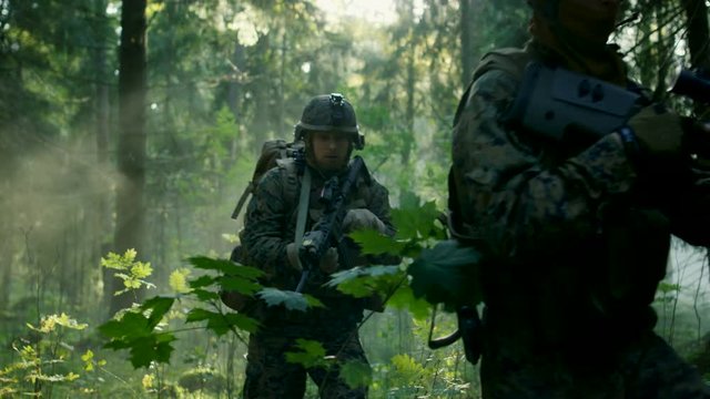 Fully Equipped Soldiers Wearing Camouflage Uniform Attacking Enemy, Rifles Ready to Shoot. Military Operation in Action, Squad Running in Formation Through Dense Smokey Forest. Slow Motion Footage. 