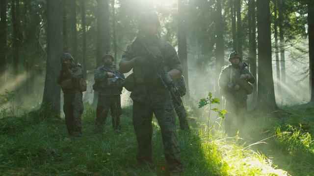 Five Fully Armed Soldiers Stand Alert with Guns Ready. Military Operations Takes Place in the Sunny Dense Forest. Shot on RED EPIC-W 8K Helium Cinema Camera.