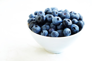 Fresh blueberries in the white ceramic bowl on a white table. 
