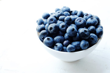 Fresh blueberries in the white ceramic bowl on a white table. 