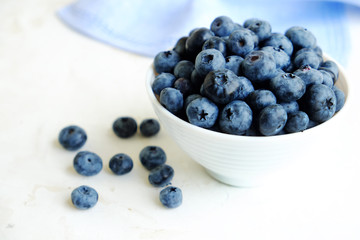 Fresh blueberries in the white ceramic bowl on a white table. 