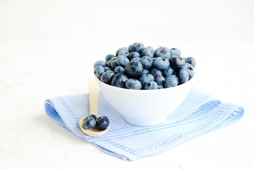 Fresh blueberries in the white ceramic bowl on a white table. 