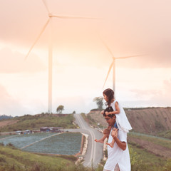 Father and daughter having fun to play together in wind turbine field and child girl riding on father's shoulders in cloudy day in vintage color tone