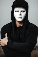 Portrait of man in black hoodie wearing white anonymous mask.