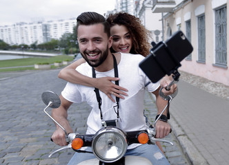 Happy couple on scooter making selfie on smartphone outdoor