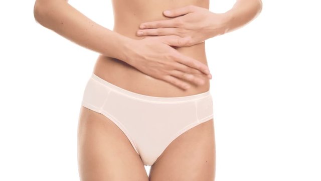 Slim woman is applying cream on her stomach. White background.