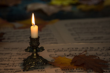 sheet music, lighted candle and autumn leaves