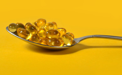 Omega-3 fish fat oil capsules in spoon on a yellow