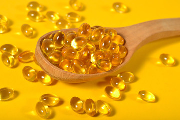 Omega-3 fish fat oil capsules in wooden spoon on a yellow