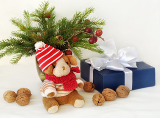 A small  toy dog in a knitted cap, gift boxes, nuts and Christmas spruce branches. Christmas and New Year card. Still life.