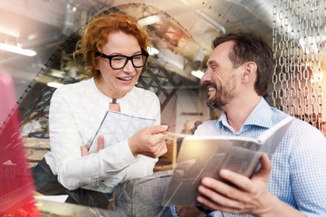 Search of approval. Handsome young man showing the notebook with his ideas in it to his female colleague while she reading them and smiling, liking the content