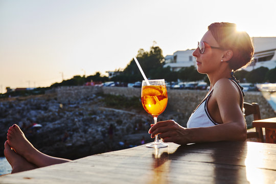 Italy, Santa Caterina, woman relaxing on promenade with glass of Spritz at sunset