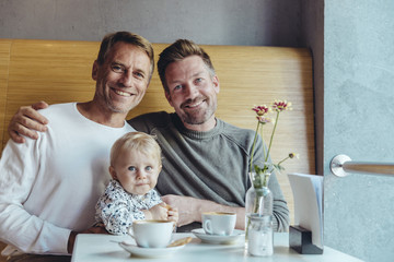 Portrait of happy gay couple with their baby in cafe