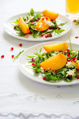 Fresh autumn salad with persimmon, arugula, cheese and pomegranate seeds on white table cloth. Space for copy
