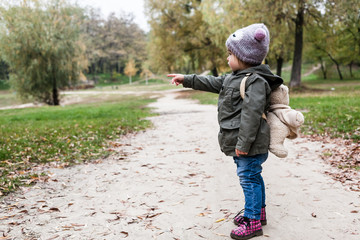 Little girl in autumn forest with teddy bear backpack.