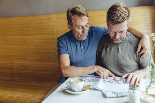 Gay couple looking at constructions plans for their home in cafe