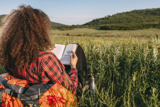 Back view of teenage girl reading book on a meadow