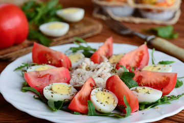 Simple vegetable salad with chicken and eggs. Healthy salad with fresh tomatoes slices, arugula, boiled quail eggs, chicken fillet and spices on a white plate. Rustic style. Closeup