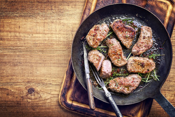 Fried saddle of pork steak with herb as top view in a frying pan with copy space left