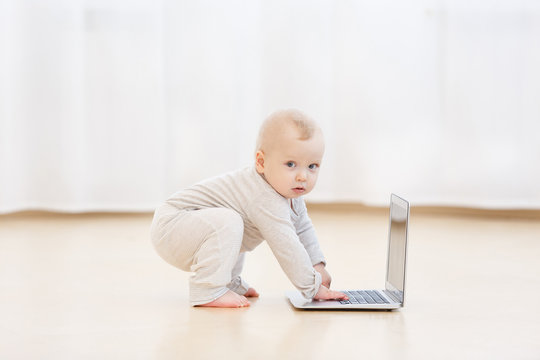 Cute baby boy in white home clothes with laptop in a light living room of the house. hobbies of children for computer, education of child