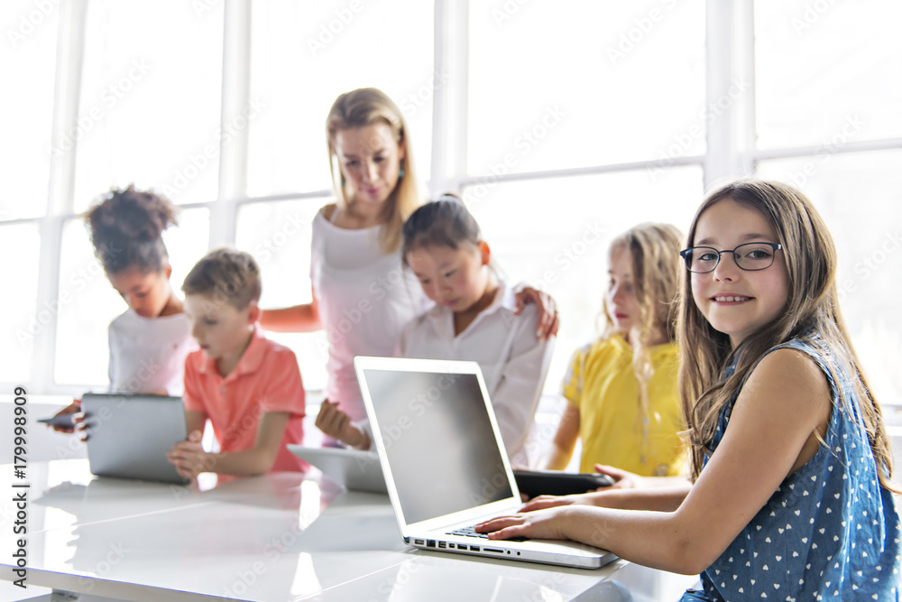 Wall mural child with technology tablet and laptop computer in classroom teacher on the background