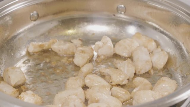 Closeup of chicken meat strips cooking on a hot pan on a gas stove. Chicken frying in a pan, Top view. Cooking fried chicken breast in oiled pan on stovetop