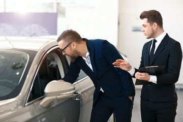 A man is examining new car's design and interior in car dealership