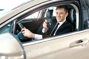 Fototapeta na wymiar Formal wearing young man behind the wheel. He is looking at camera, showing the car key and smiling.