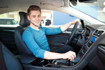 Young man or student behind the wheel. He is looking at camera and smiling.