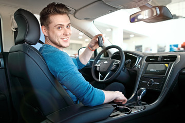 Naklejka premium Young man or student is sitting in car, smiling and showing the car key.
