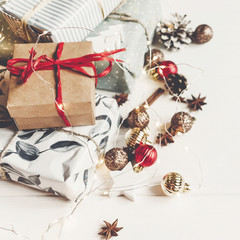 wrapped present boxes with ornaments pine cones anise and lights on white wooden background top view, space for text. merry christmas concept. seasonal greetings card. happy holidays