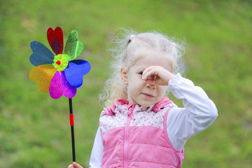 Little curly blonde girl holding multicolored pinwheel in her hands.