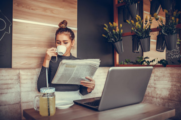 Beautiful young woman reading newspaper and drinking coffee  in coffee shop