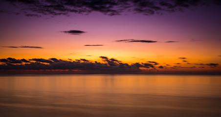 Stylized abstract landscape seascape sunset long exposure with clouds under different shades of blue, orange, yellow and red.