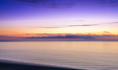 Stylized abstract landscape seascape sunset long exposure with clouds under different shades of blue, orange, yellow and red.