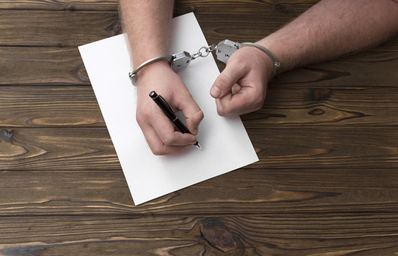 The hands of the criminal in handcuffs write with a pen on paper. A sincere confession. request. statement.