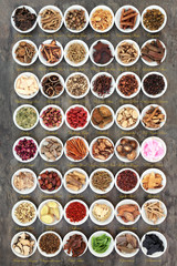 Large chinese herb collection in white porcelain bowls used in traditional herbal medicine on marble background with descriptive titles.