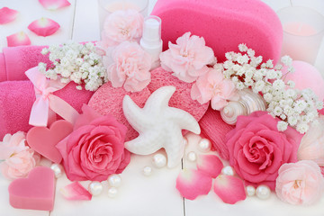 Beauty spa treatment and cleansing products with pink roses and carnation flowers, body lotion, starfish seashell soap, sponges, wash cloths with seashells and pearls on white wood background.