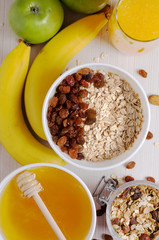 Healthy Breakfast. Oatmeal with raisins in white bowl. Two green apples, bananas, honey, nuts, granola