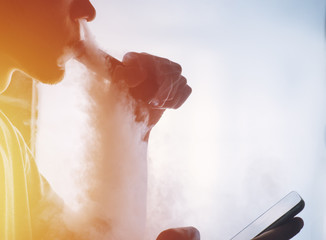 a bearded man smokes e-cigarette mechanical mod and uses the smartphone in your hand