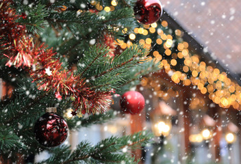 Christmas street decorations and falling snow - red ball, fir and bokeh lights