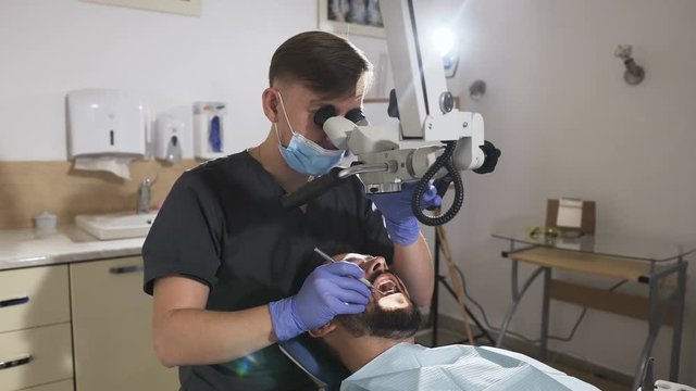 Doctor dentist using dental microscope in modern dental office for operation. Male dentist with dental tools - microscope and mirror